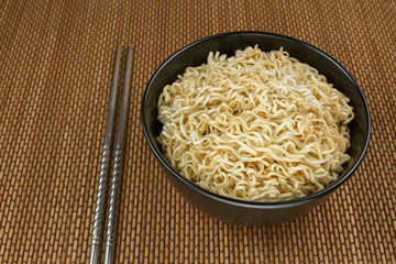 Instant noodles in a black bowl on Japanese mat and chopsticks