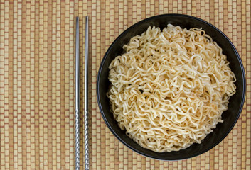 Instant noodles in a black bowl on Japanese mat and chopsticks