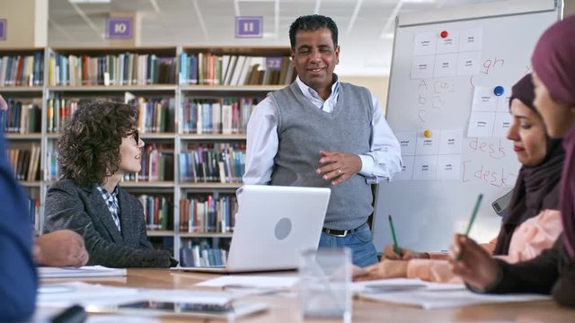 Mid-aged arab man standing at flipchart and explaining English grammar to group of migrant students