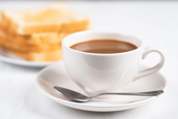 Cup of coffee and sliced bread on white table, breakfast