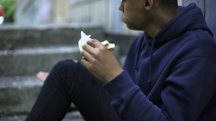 Homeless orphan boy eating sandwich alone, poverty problem, charity donation