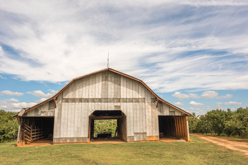 An old, beautiful barn that holds farm equipment stands regally on the side of the road in rural,...