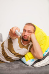 Man sitting on couch while switching TV channels. Focus on remote control.
