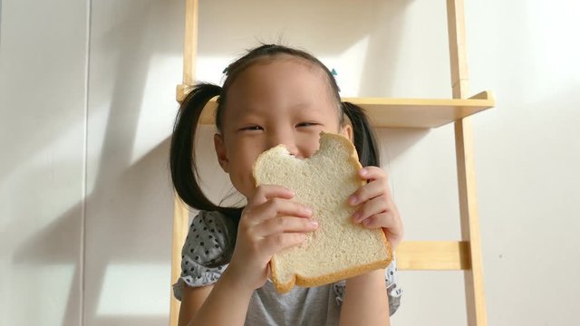Little asian girl eating bread for breakfast at home
