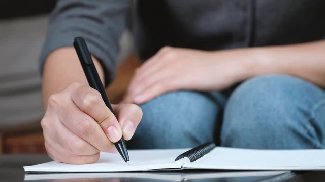 A woman's hand writing down on a white blank notebook on table