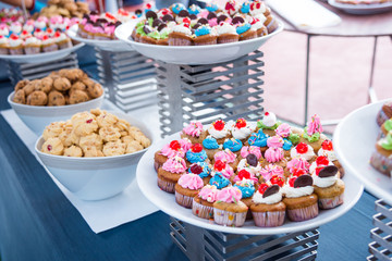 Many tasty colorful cupcakes on white plate and many sweet at party