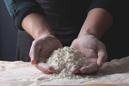 Hands of cook with flour on a dark background.