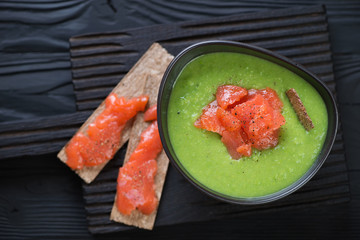 Green peas cream-soup with addition of salmon over black wooden background, above view, studio shot