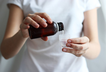 Female hand pour cough syrup in a measuring cup on a light background. The concept of health. 