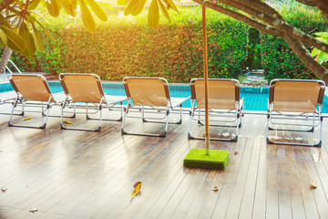 Rear view of sun loungers on wooden decks at the side of swimming pool. For relaxation and...