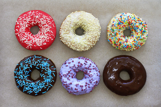 Donuts of different colors on cardboard, view from above 