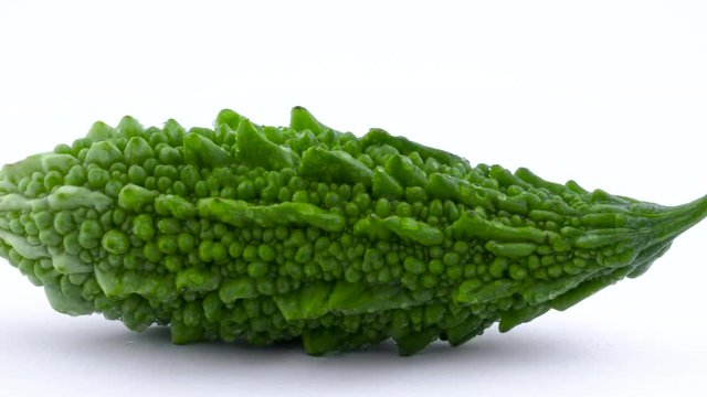 Macro shooting of whole green bitter melon with water drops. Cross cut. Rotating on the turntable isolated on the white background. Close-up.