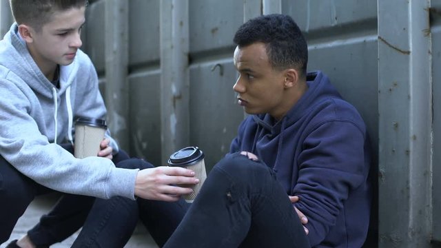 Boy sharing warm coffee with frozen homeless teenager, charity volunteer