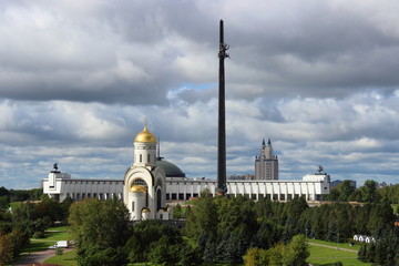 Moscow, Russia - day view to the Park Pobedy at poklonnaya hill - victory park, church, stele and monument meseum in autumn against green trees and overcast sky with heavy clouds
