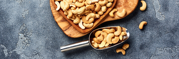 Roasted cashew nuts and scoop on gray background. Top view.