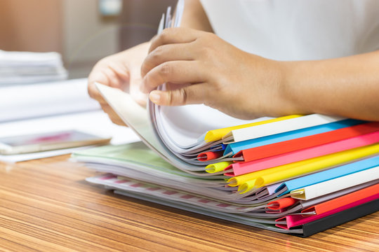 Teacher is searching for homework assignment documents with colourful sliding bar report cover of student on the teacher's desk. Paperwork pile print document organized put on the table.