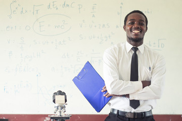 Africanman science teacher smiling in the classroom with microscope.