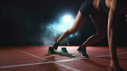 Young woman athlete in black shorts and a t-shirt is preparing to start in the race for 100 meters on the treadmill near the start line