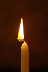 tiny paraffin burning candle with vivid flame on the heavy black background.