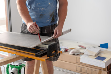 The tiler measures and puts marks to cut and lay a tile. Home renovation.