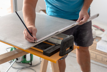 Man hands marking tile to be cut. Laying ceramic floor tiles, home renovation.