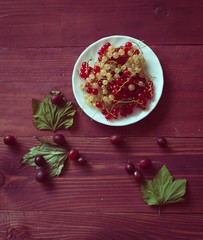 Berries of a currant, gooseberries on a saucer, leaves, on a natural wooden background