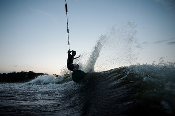 Young wakesurfer riding on blue river waves with splashes