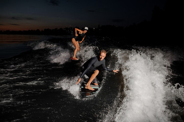 Two wake surfers riding down the blue river at the evening