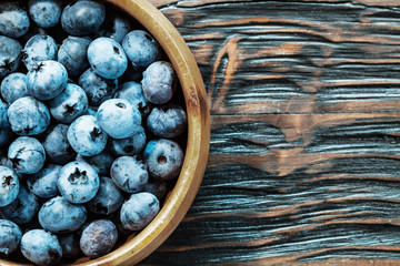Blueberries in round wooden bowl on wood board top view