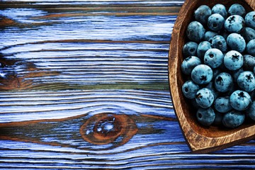 Huckleberries in heart-shaped wooden bowl on wood board