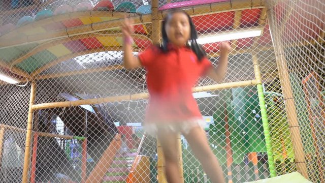 asian child cute or kid girl playing and jump on trampoline for happy fun and enjoy with smile on summer holiday relax and exercise at playground or amusement park on slow with wear red shirt