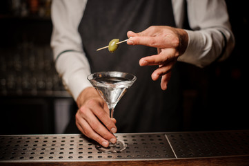 Barman decorating a fresh and strong summer martini cocktail with olive