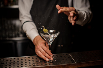 Bartender making a fresh and strong summer martini cocktail with olive and salt