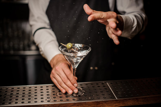 Barman making a fresh and strong summer martini cocktail with olive and salt