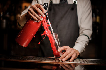 Barman pouring alcoholic sparkling water into a sweet red berry summer cocktail