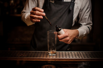 Fototapeta na wymiar Barman adding brown bitter into a cocktail glass