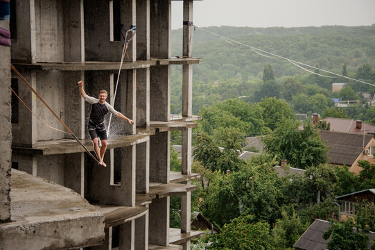 Fearless young man balancing on a slackline against building