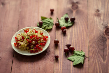 Berries of a currant, gooseberries on a saucer, leaves, on a natural wooden background