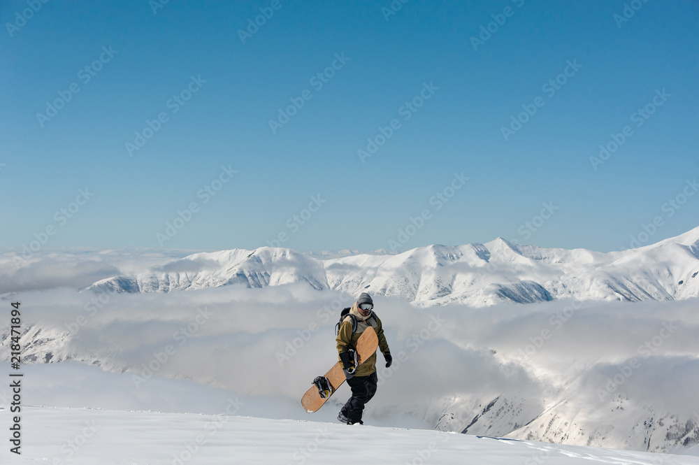 Wall mural male wearing glasses and snowboard walking in the snow against the backdrop of the mountains