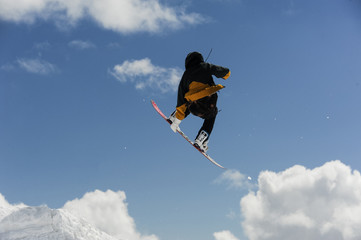 male athlete jumping with snowboard high against a blue sky and white clouds