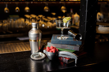 Cocktail glass with lime slice and bar utensils arranged among books