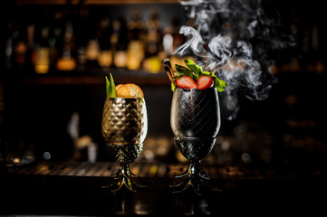 Two glasses with fresh summer cocktails decorated with fruit on the bar counter
