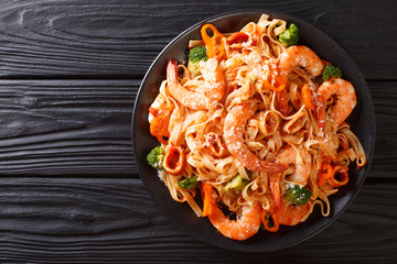 Pasta fettuccine with squid, tiger shrimps, vegetables, parmesan cheese and tomato sauce close-up...