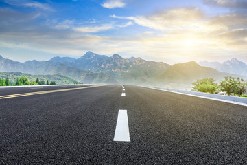Straight asphalt highway and green mountain nature landscape at sunset