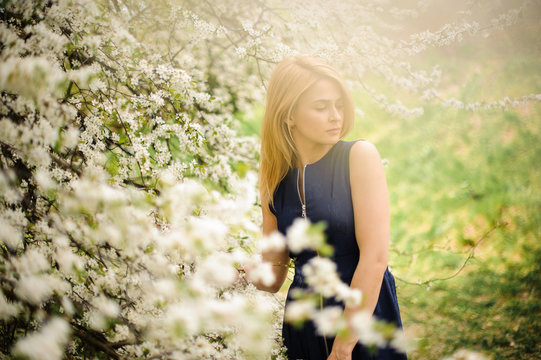 Attractive blonde woman standing on the blurred background of a white blooming cherry tree