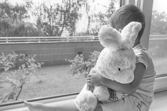 boy of two years sitting by the window and hugs a toy Bunny. rainy weather, waiting for dad to come home from work.