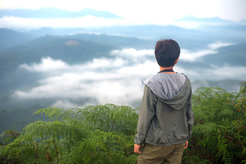 Naklejka premium Tourist woman standing on peak of mountains and enjoy view with beautiful mist and sunrise from her success at Gunungsilepat mountains, Yala province south of Thailand.