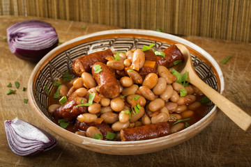 Beans stew wit pork sausages and tomato sauce on table with onion