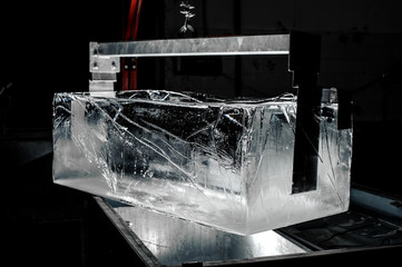 Steel tool holding a huge ice cube on dark background of modern factory