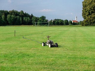Mobile sprinkler on an empty soccer field on the countryside in the dry summer time © Alex